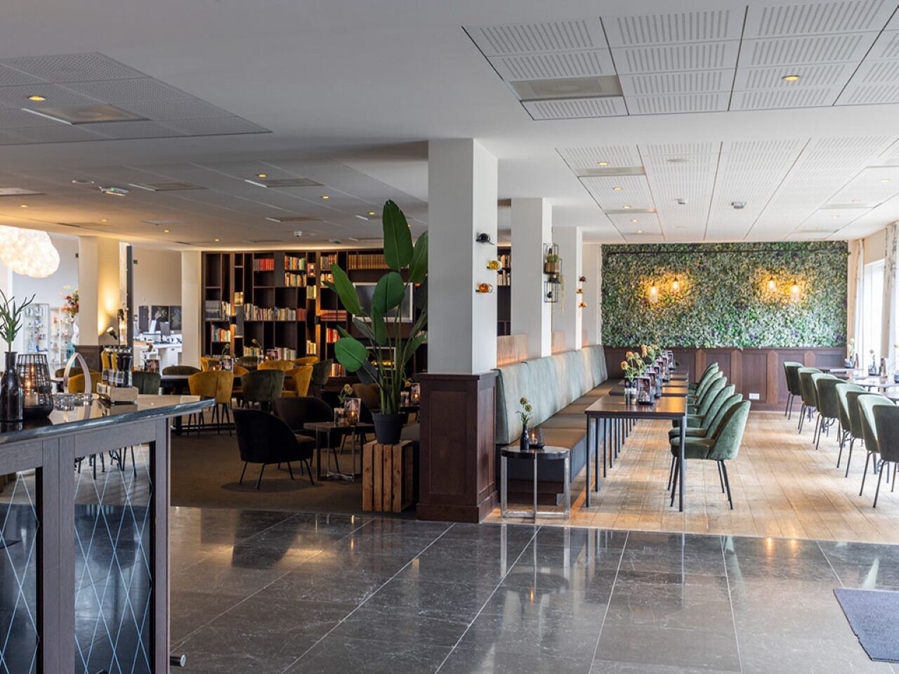 Um hall de hotel moderno com um balcão de recepção extenso, área de estar e uma parede com padrão de folhas.