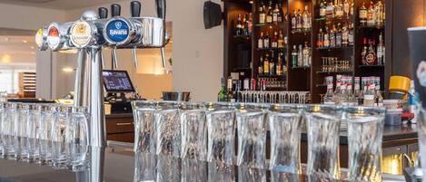 A bar area with multiple beer taps, a well-stocked liquor shelf, and a row of empty glasses.