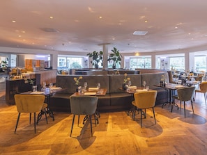 A spacious restaurant with a central seating area, multiple tables, and a wooden floor.