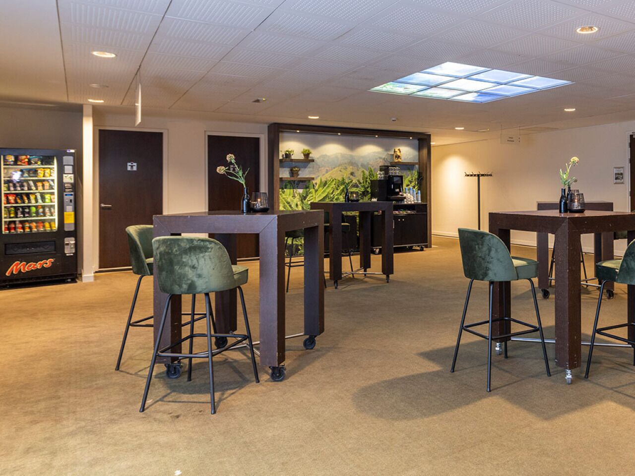 A hotel lobby with a vending machine, bar stools, a reception desk, and a wall with a plant display.