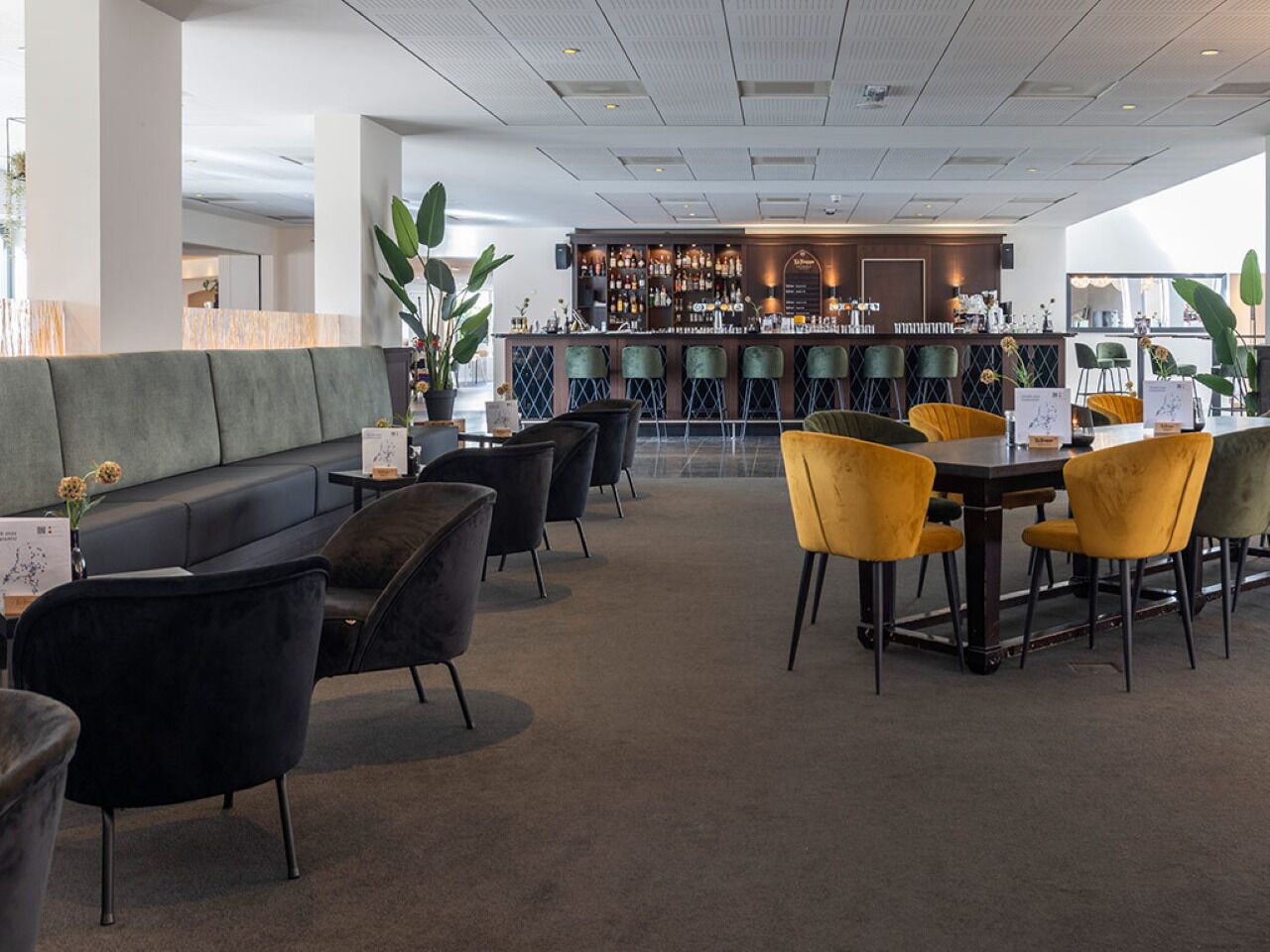 A modern bar area with a seating arrangement of sofas and chairs, a bar counter, and a large window providing natural light.