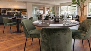 A dining area with a round table, green upholstered chairs, and a large potted plant.