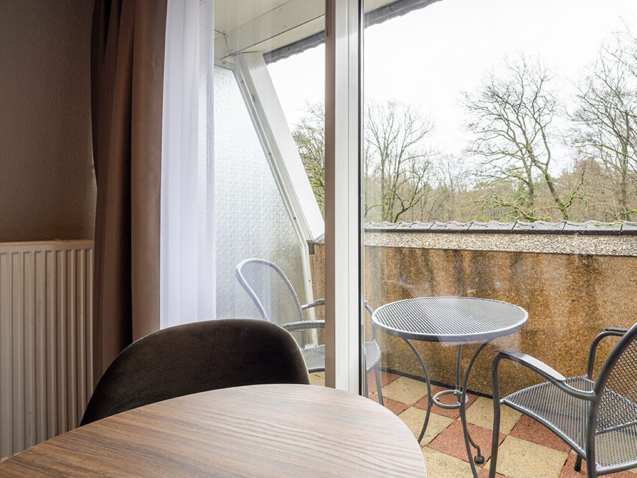 Un balcone con tavolo e sedie, vista su alberi e un edificio sullo sfondo.