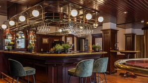 A bar area with a wooden bar, three bar stools, a chandelier, and a fish tank. - Doorwerth Hotel-Style Stay in Nature Near Arnhem & Hiking Trails - 3 Units (Doorwerth)