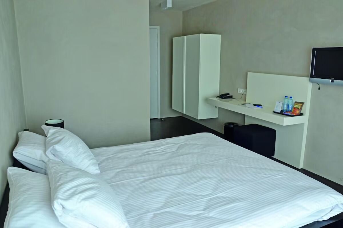 Ein Hotelzimmer mit einem Bett, einem Schreibtisch mit Computer, einem Fernseher und einem Spiegel.