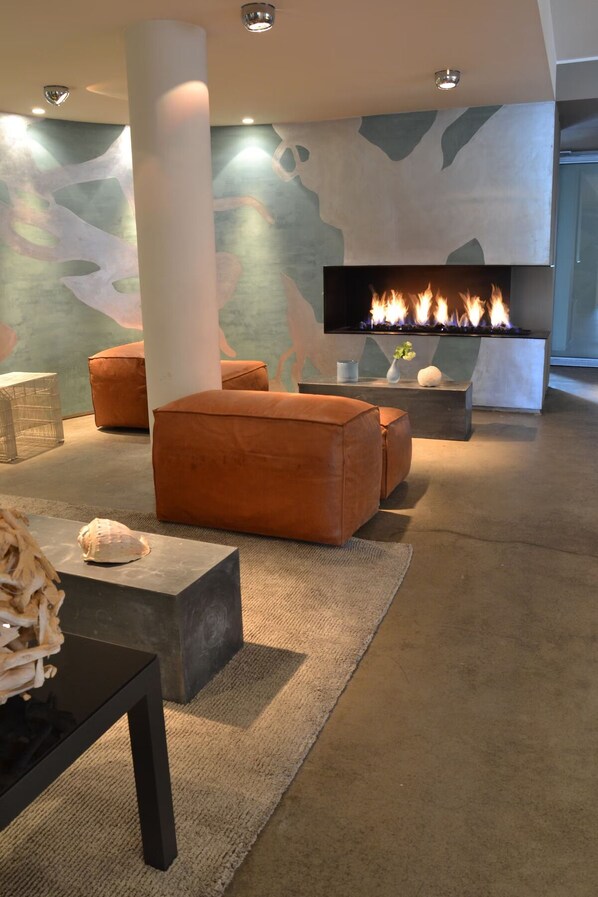 Una sala de estar moderna con chimenea, otomanas de cuero, una mesa de piedra y arte abstracto en la pared.