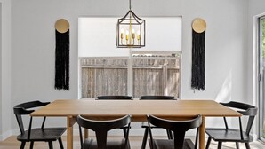 Een eetgedeelte met een houten tafel en zwarte stoelen, een hanglamp en uitzicht door een raam met een houten hek.
