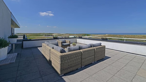 Une terrasse sur le toit avec un canapé en osier, des sièges d’extérieur et une vue sur la mer.