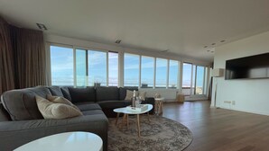 Un salon moderne avec un canapé d’angle gris, une table basse ronde et un téléviseur à écran plat fixé au mur.