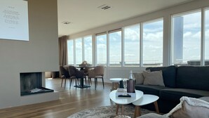 Un salon moderne doté d’une cheminée, d’un coin repas et de grandes fenêtres offrant une vue sur le ciel.