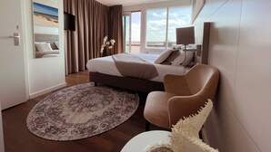 Une chambre d’hôtel moderne, équipée d’un lit, d’une chaise, d’un tapis rond, d’un téléviseur et d’une grande fenêtre.