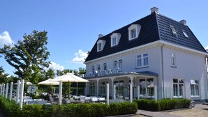 Un bâtiment sur lequel on peut lire l’inscription « Restaurant DUNZICHT », avec une terrasse extérieure dotée de parasols et une zone recouverte de gravier à l’avant.