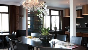 Un espace repas comprenant une table ronde, des chaises, un lustre et un vase rempli de fleurs blanches.