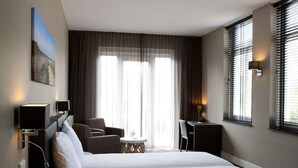 Habitación de hotel con cama, dos sillas, un escritorio, una lámpara y un cuadro en la pared.