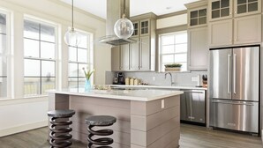 Een moderne keuken met een centraal eiland, roestvrijstalen apparatuur en een hangende lamp.