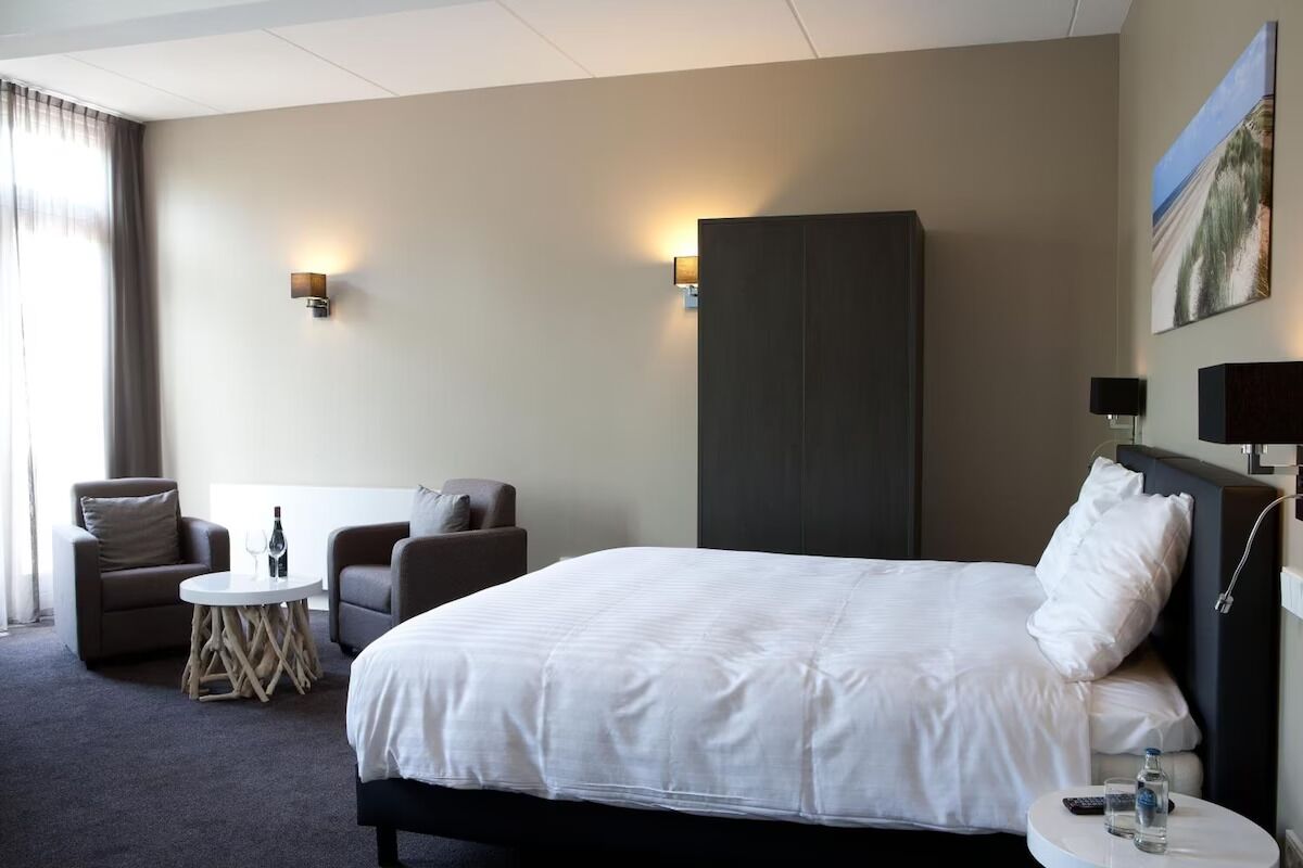Une chambre d’hôtel avec un grand lit, deux fauteuils, une petite table ronde et une armoire.