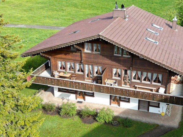 A two-story wooden house with a balcony, large windows, and a chimney. - Chalet Rotebächli by Interhome (Lenk)