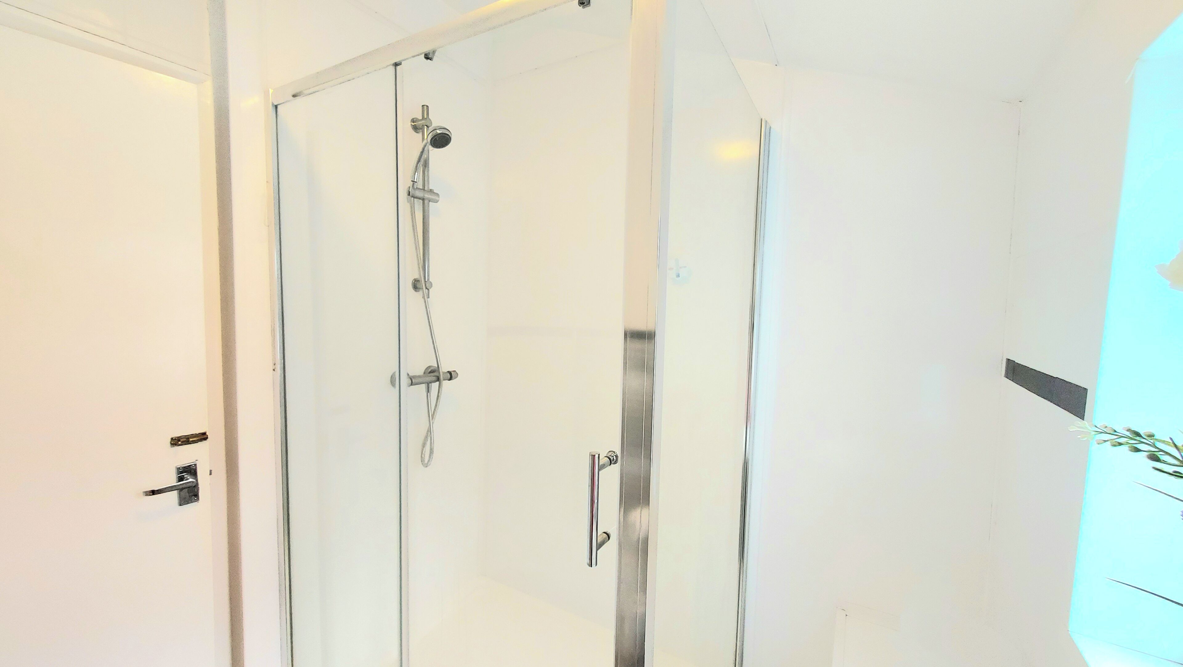 Ein modernes Badezimmer mit Duschkabine aus Glas, einer weißen Wand und einer Tür mit Griff.