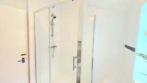 Une salle de bain moderne avec une douche à parois de verre, un mur blanc et une porte dotée d’une poignée.
