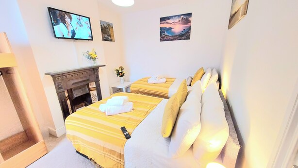 A hotel room with two beds, a fireplace, a TV, and artwork on the walls.