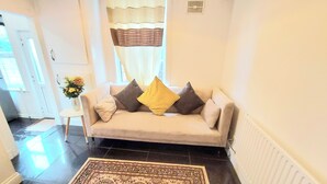 A living room with a beige sofa, a patterned rug, and a vase with flowers.