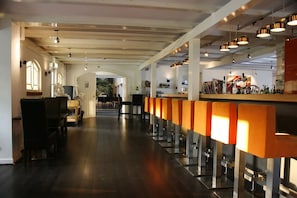 Un espace bar doté d’un long comptoir, de chaises et de luminaires suspendus.