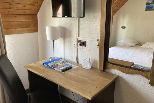 Une chambre d’hôtel avec un bureau en bois, un téléviseur fixé au mur, un lit avec une literie blanche et un miroir qui reflète le lit.