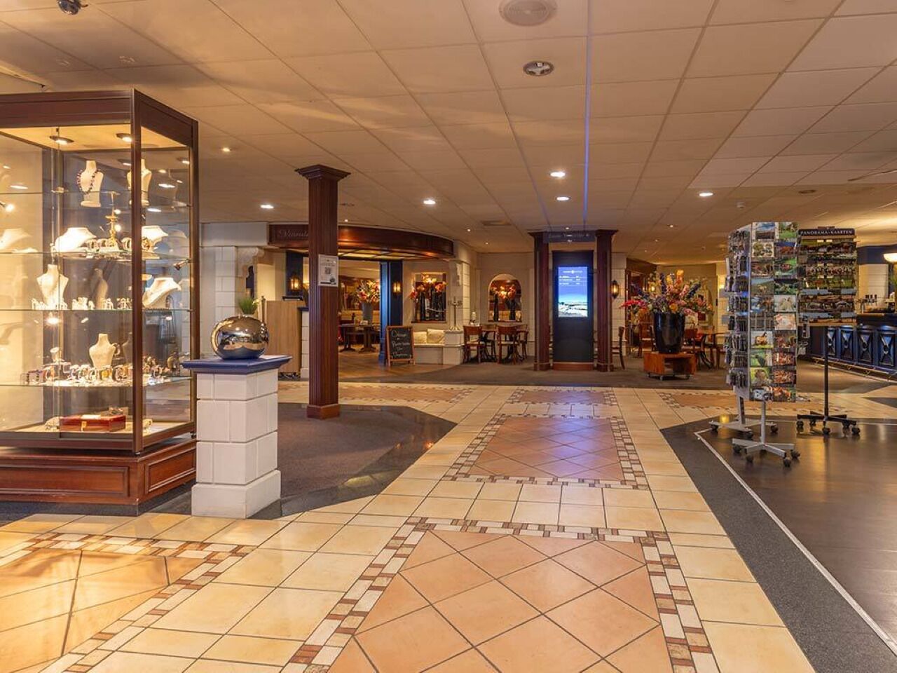 A hotel lobby with a tiled floor, a jewelry display, a seating area, and a gift shop.