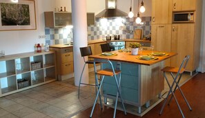 A modern kitchen with a central island, bar stools, a stove, and a microwave.