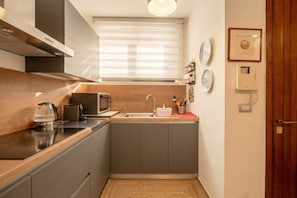 Uma cozinha compacta com micro-ondas, chaleira e torradeira, uma janela com persianas e uma porta com painel de madeira.