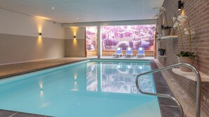 An indoor swimming pool with clear water, a metal pool ladder, and a view of a forest through large windows.