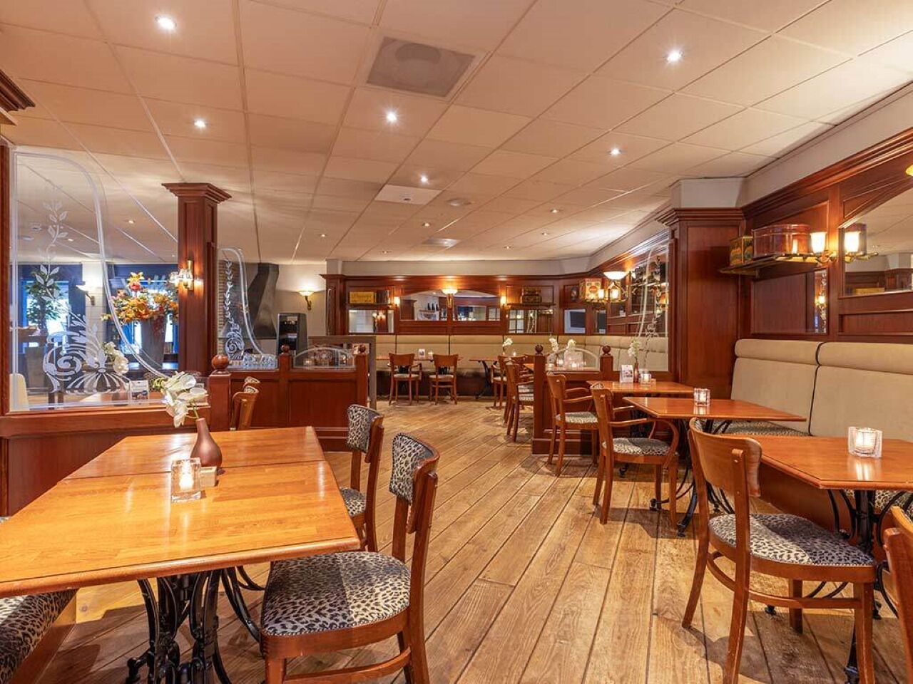 A restaurant with wooden tables and chairs, a bar area, and a view through the window.