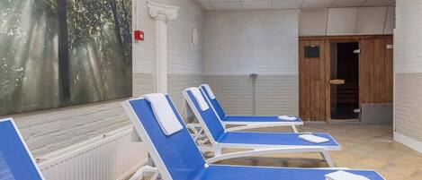 A room with four blue lounge chairs, a large window with a forest view, a skylight, and a wooden door.