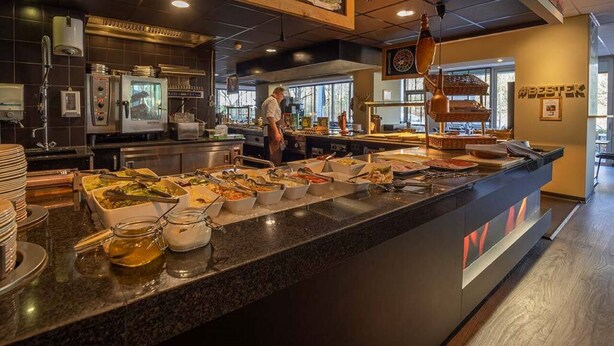 A buffet setup with various food items, a chef preparing food, and a sign with text in a foreign language.