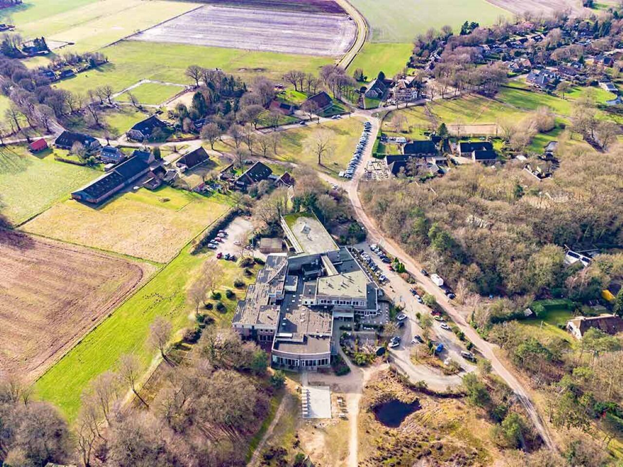 An aerial view of a large estate with multiple buildings, including a central structure with a curved roof, surrounded by open fields and smaller houses.