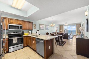 A modern kitchen with a central island, a dining area with a view, and a living space with a ceiling fan. - Ariel Dunes I 1708*Beach access and 3 pools! (Miramar Beach)
