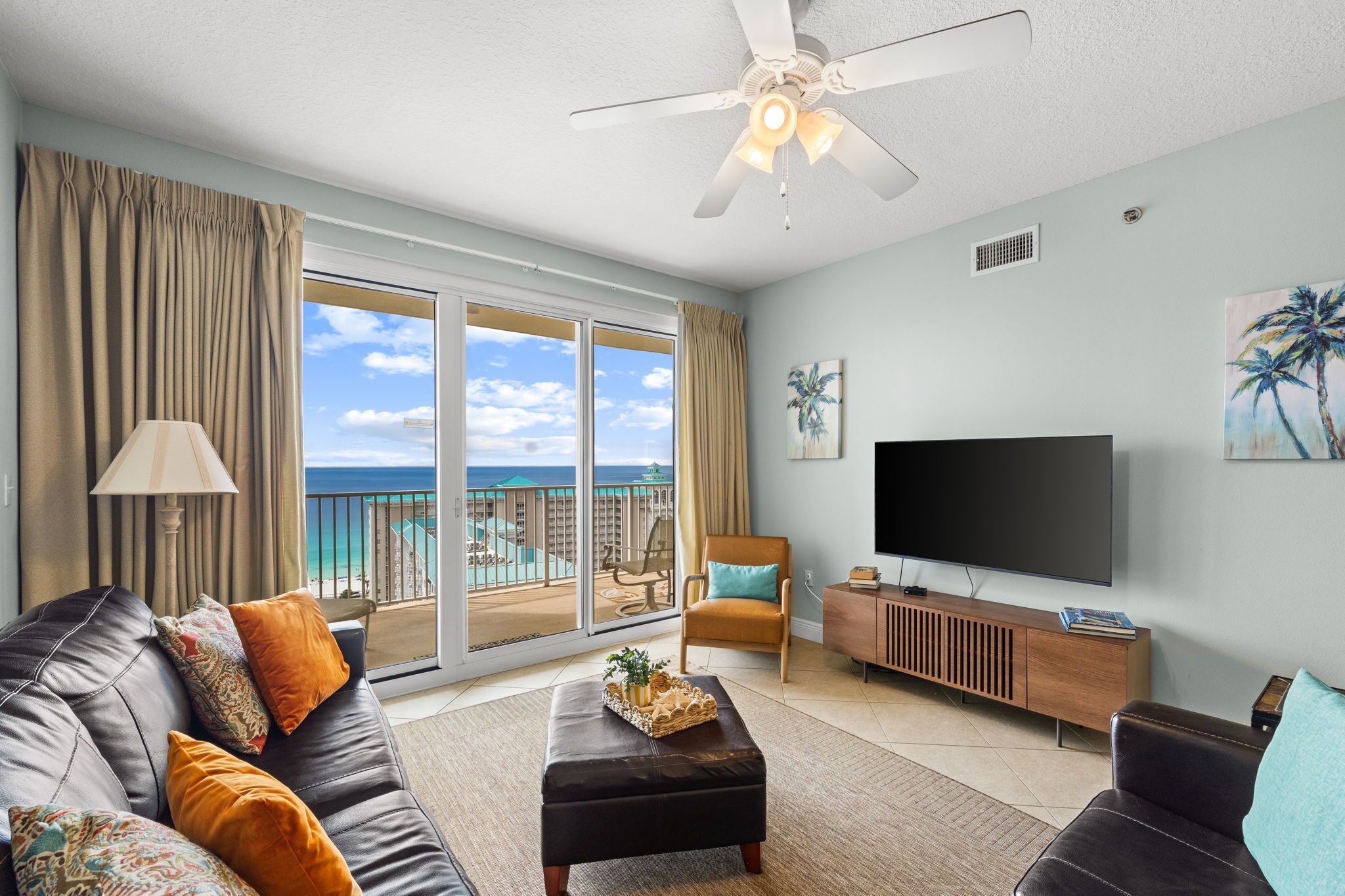 Un salon comprenant un canapé, un pouf, une télévision et un balcon avec vue sur l’océan.