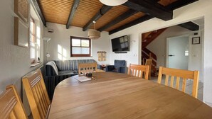 A dining area with a large wooden table, chairs, a sofa, a television, and a staircase. - Our Knüllperle half timbered holiday home next to Silbersee lake in Frielendorf (Frielendorf)