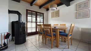 A dining area with a table, chairs, a stove, and a window with blinds. - Our Knüllperle half timbered holiday home next to Silbersee lake in Frielendorf (Frielendorf)