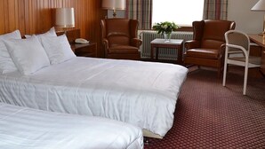 A hotel room with a large bed, two chairs, a small table, and a window with curtains.