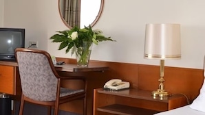 A hotel room with a bed, a desk with a chair, a telephone, a lamp, a mirror, and a television.
