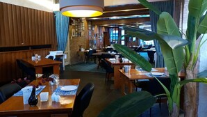 L’intérieur d’un restaurant avec des tables et des chaises en bois, un luminaire suspendu et une grande plante.