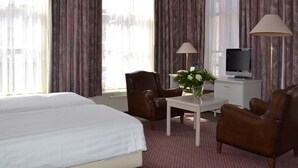 Une chambre d’hôtel avec deux lits, un bureau avec une lampe, une chaise, une télévision et des rideaux.