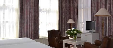A hotel room with two beds, a desk with a lamp, a chair, a TV, and curtains.