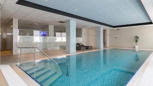 Una piscina interior con agua cristalina, paredes revestidas de azulejos y un diseño moderno.