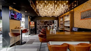 Zona de bar con mostrador de madera, sillas de cuero, candelabro y pantalla de televisión.