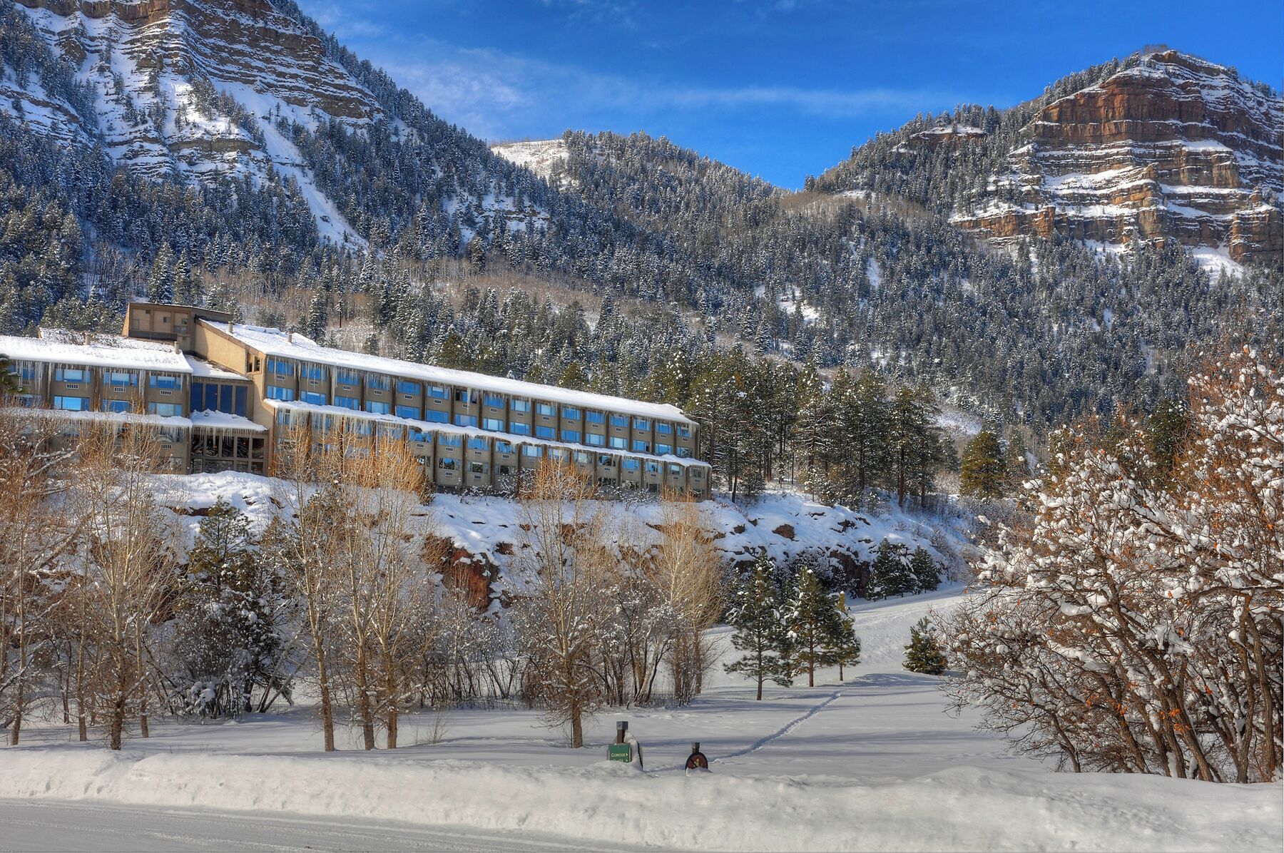 A hotel with a modern design, surrounded by snow-covered mountains and trees.