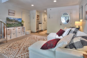 A living room with a sofa, a rug, a television, and a kitchen in the background.