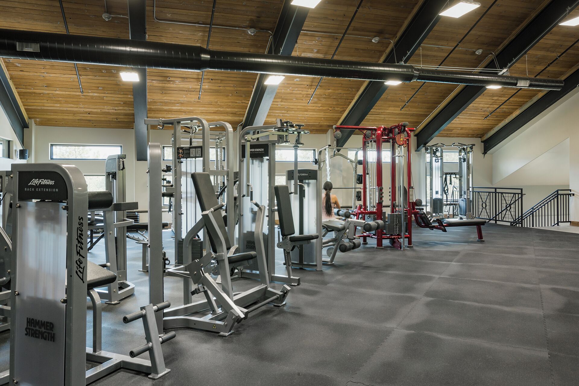 A gym with various exercise machines, a wooden ceiling, and a large window.