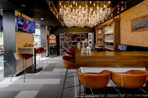 Zona de bar con mostrador de madera, sillas de cuero, candelabro y pantalla de televisión.